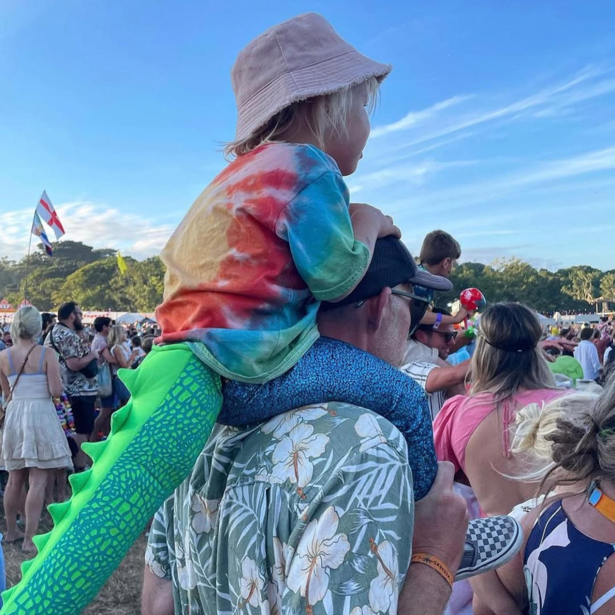 Child on adult’s shoulders at a family-friendly music festival, wearing bright blue disco leggings.