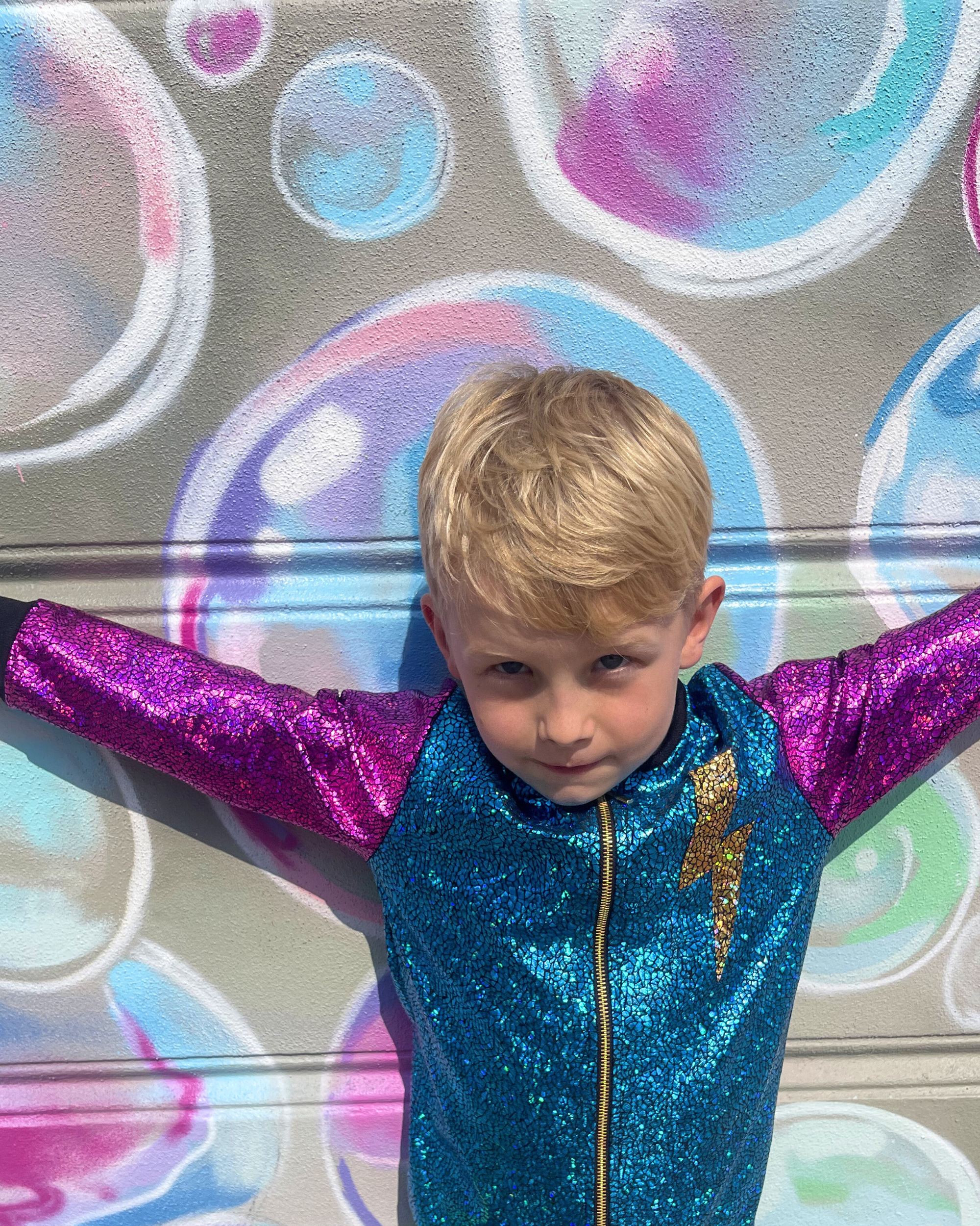 Child wearing a colorful outfit with arms outstretched in front of a bubble art background